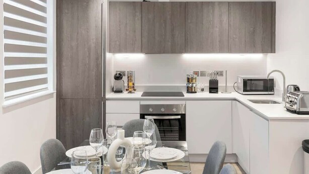 Una cocina moderna con armarios grises, horno empotrado, microondas y comedor con sillas y mesa dispuesta para una comida.
