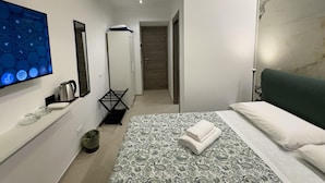 A modern hotel room with a bed, a TV, a kettle, a drying rack, and a marble wall.