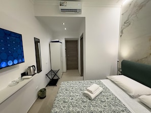 A modern hotel room with a bed, a TV, a kettle, a drying rack, and a marble wall.