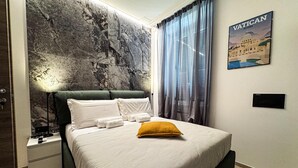 A bedroom with a bed, a nightstand, a lamp, a wall with a marble-like texture, and a framed picture of Vatican Rome. - VATICAN ROOMS DORIA  (Rome)