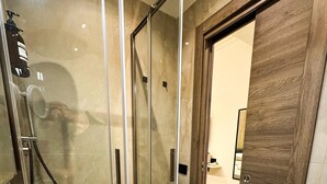 A bathroom with a glass-enclosed shower, a white sink with a modern faucet, and a wooden door.