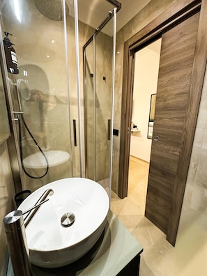 A bathroom with a glass-enclosed shower, a white sink with a modern faucet, and a wooden door.