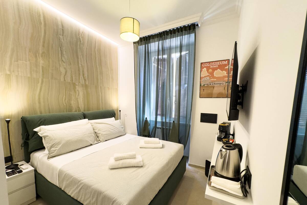 Una habitación de hotel con una cama, una mesita de noche, una cafetera y un cartel del Coliseo.