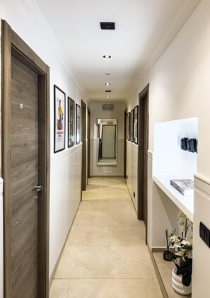 A hallway with framed pictures on the walls, a white reception desk, and a door on the left. - VATICAN ROOMS DORIA  (Rome)