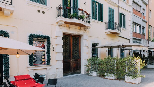 A building with a wooden door, green shutters, and outdoor seating with umbrellas. - VATICAN ROOMS DORIA  (Rome)