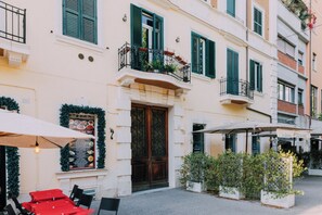 A building with a wooden door, green shutters, and outdoor seating with umbrellas. - VATICAN ROOMS DORIA  (Rome)