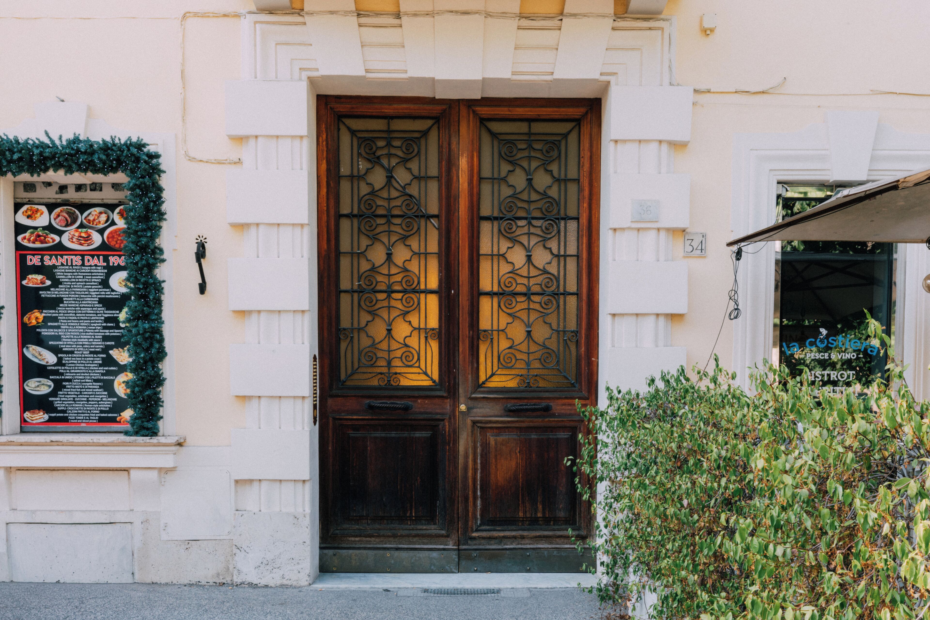 A building entrance with a double wooden door, a Christmas wreath, and a menu board.
