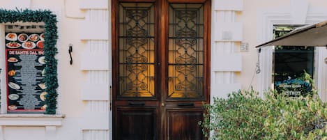 A building entrance with a double wooden door, a Christmas wreath, and a menu board.