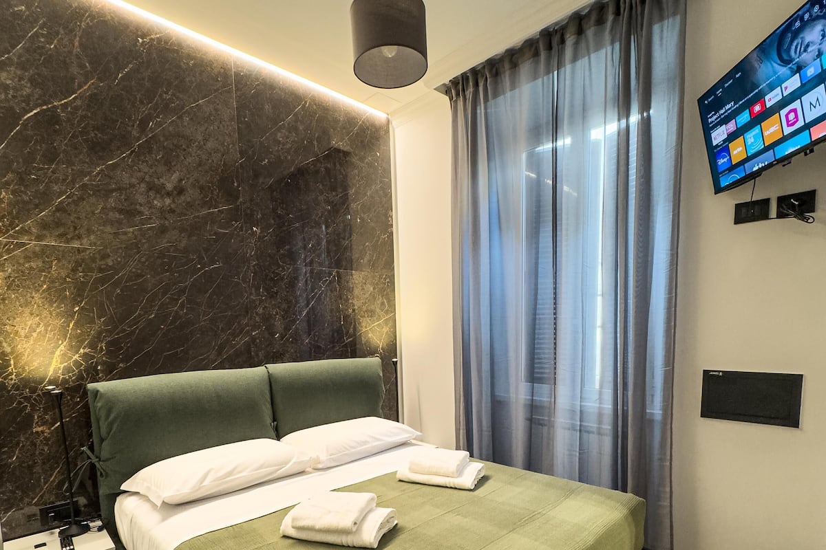 Una habitación de hotel moderna con una cama grande, un televisor de pantalla plana en la pared y una pared decorativa de mármol.
