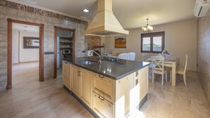 A kitchen with a central island, a dining area with a table and chairs, and a view of the outdoors through a window.