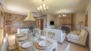 A dining area with a table set for four, a kitchen with a stove and cabinets, and a living area with a sofa and a fireplace.