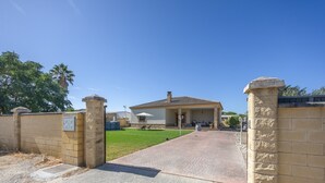 A gated entrance to a property with a paved driveway leading to a covered patio area with outdoor seating.