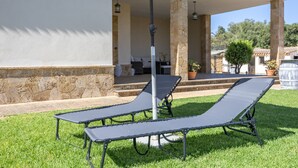 Two lounge chairs under an umbrella, a stone wall, and a patio area with a table and chairs.