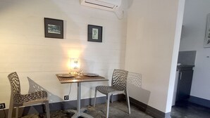 Una habitación pequeña con una mesa y dos sillas, un aire acondicionado de pared y dos cuadros enmarcados.