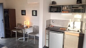 Una cocina compacta con refrigerador, microondas, pileta y estantes con vajilla.