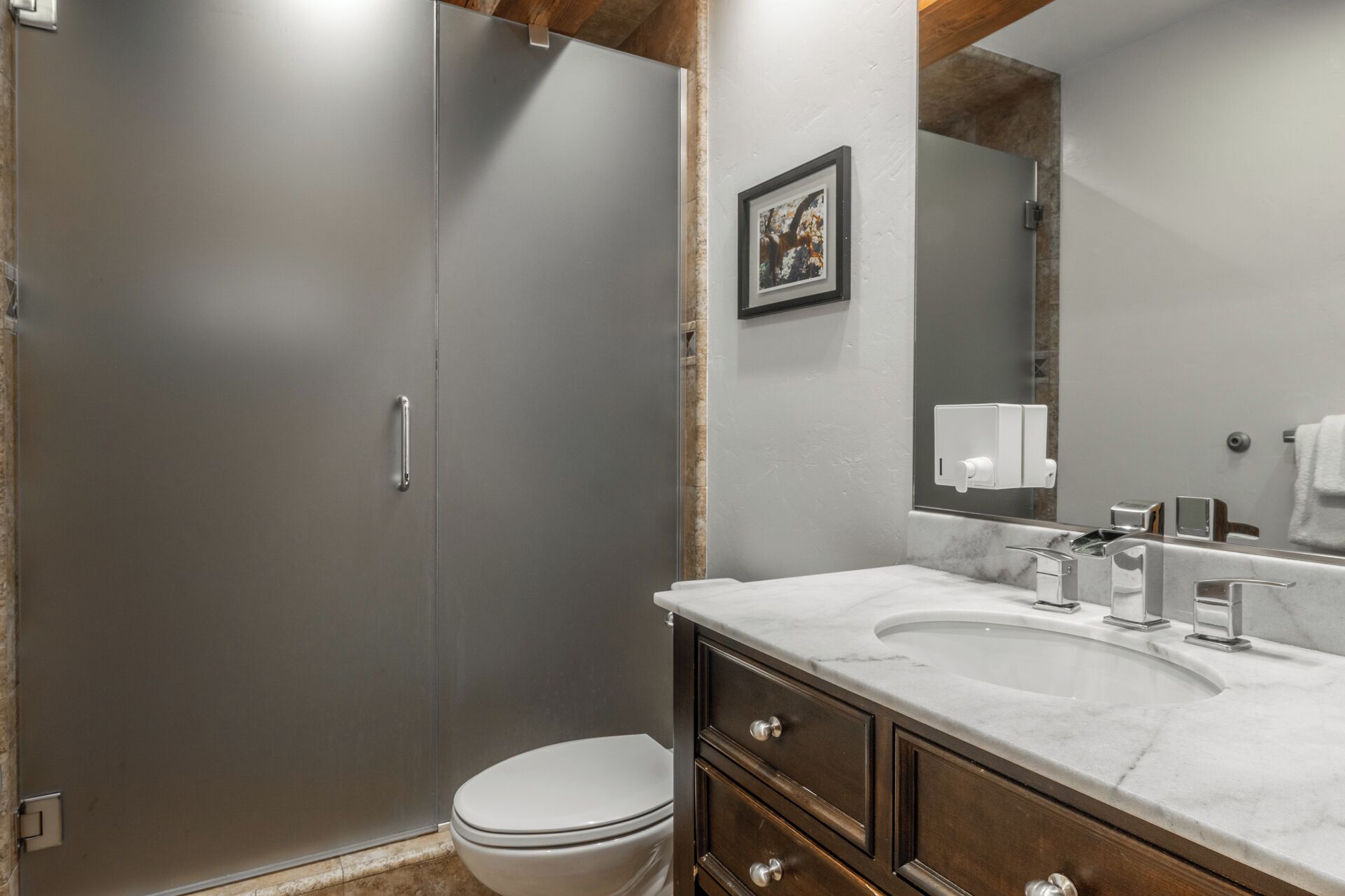 A bathroom with a toilet, a shower, a sink with a marble countertop, and a mirror.