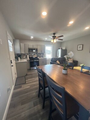 A modern kitchen with a dining area, a ceiling fan, and a view of the city. - Whispering Pines Cottage (Egg Harbor City)
