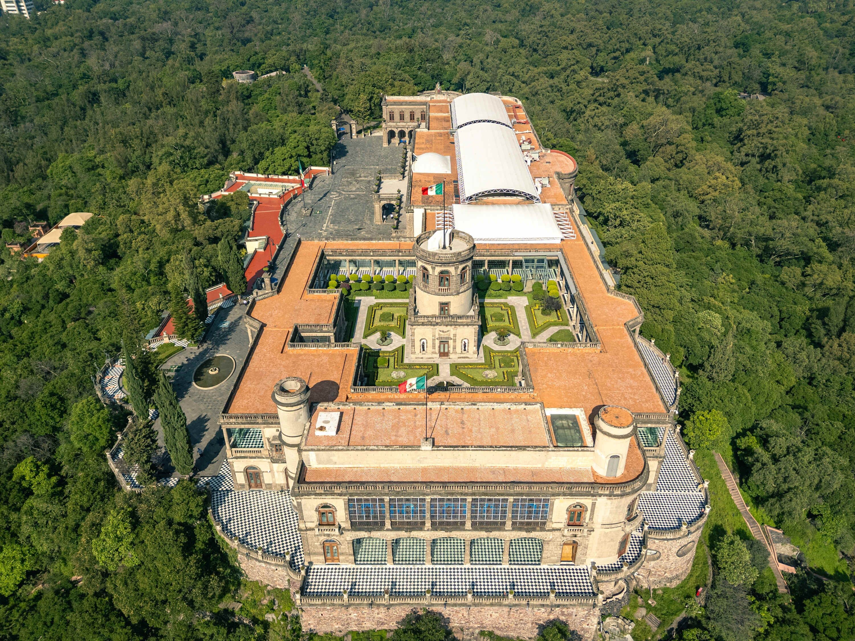 An aerial view of a historic building with a central courtyard, surrounded by lush greenery.