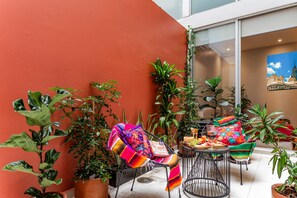 An outdoor patio with potted plants, a table set for dining, and a chair with a colorful blanket. - Colorful Roma Norte 3BR/3BA, 2 patios, AC (Mexico City)
