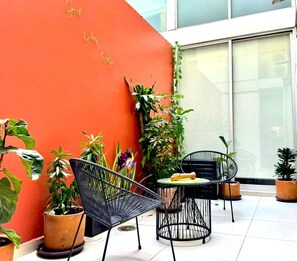 A patio area with a red wall, potted plants, and two black chairs. - Colorful Roma Norte 3BR/3BA, 2 patios, AC (Mexico City)