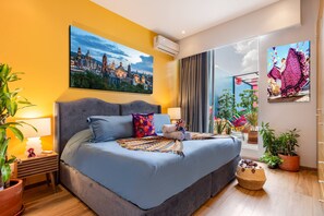 A modern hotel room with a large bed, a cityscape painting, and a vibrant artwork on the wall. - Colorful Roma Norte 3BR/3BA, 2 patios, AC (Mexico City)
