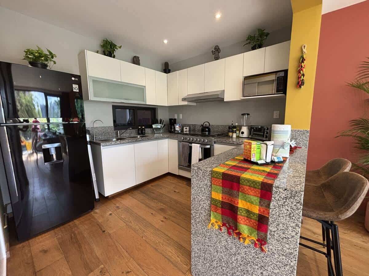 A modern kitchen with white cabinets, a granite countertop, a black refrigerator, and a colorful table runner.