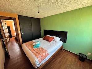 Une chambre d’hôtel avec un lit, une tête de lit, un mur vert, un plancher en bois et un plafond à motifs.