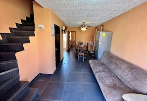 Un couloir avec un escalier, un canapé, une table à manger avec des chaises et un réfrigérateur.