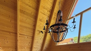 Un intérieur en bois avec un plafond haut, un lustre, un canapé gris, un fauteuil jaune et une grande fenêtre.