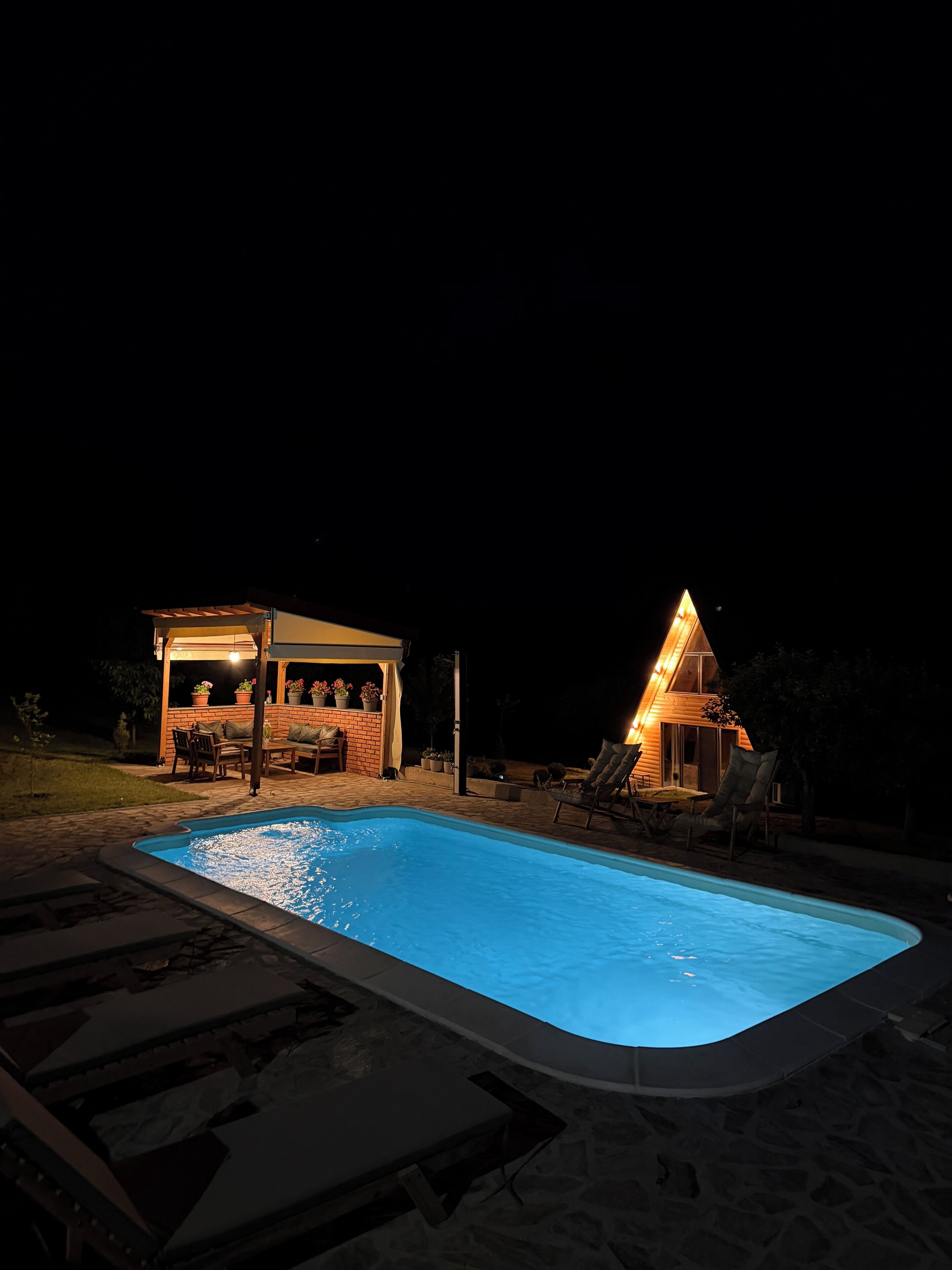 A swimming pool with a covered patio area, a small building, and a triangular structure.