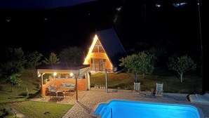 Une maison avec une piscine, un patio couvert et un éclairage extérieur bien étudié pour la nuit.