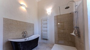 Een moderne badkamer met een vrijstaand bad, een douche met glazen wanden en een witte handdoekhouder.