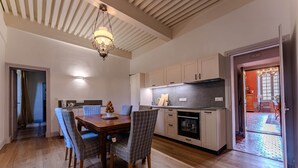 Ein Essbereich mit Holztisch und Stühlen, einer Chandelierleuchtre und einer Küche mit Schränken und Geräten.
