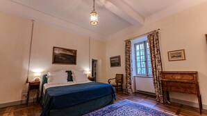Ein Schlafzimmer mit einem Bett, einem Sessel, einem Holztisch und einem Fenster mit Vorhängen.