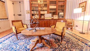 Een kamer met een ronde houten tafel, twee stoelen, een grote boekenkast en een kamerkleed met patroon.