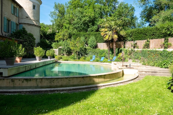 A swimming pool with a curved edge, surrounded by a grassy lawn and potted plants.