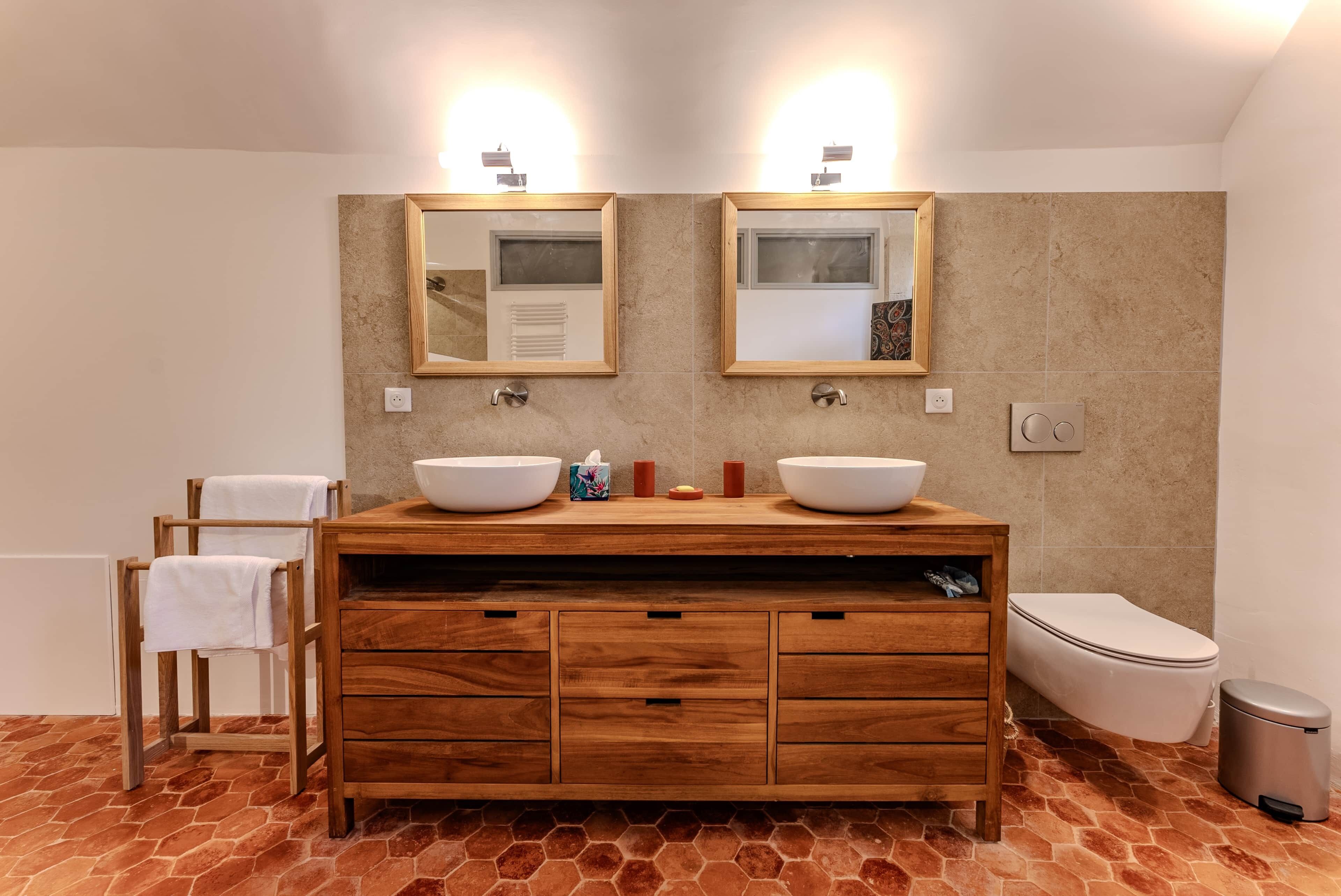 Ein Badezimmer mit zwei Waschbecken, einem Holz-Vanity-Schrank, Spiegeln und einer Toilette.