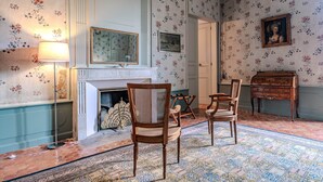 Een kamer met een open haard, behang met een patroon en een houten dressoir.