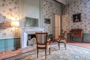 A room with a fireplace, patterned wallpaper, and a wooden dresser.