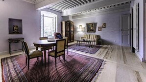 A room with a dining table, chairs, a sofa, a patterned rug, a cabinet, and a door. - Tour Est Vacation Rental at Château de Vachères. (Montclar-sur-Gervanne)