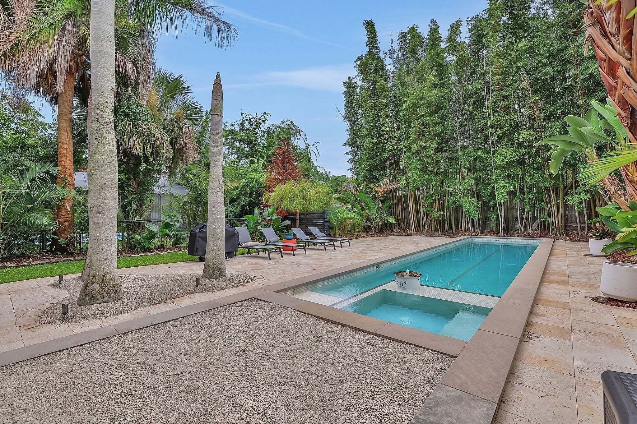 Ein rechteckiger Swimmingpool mit einer gefliesten Terrasse, umgeben von Kies und Palmen.