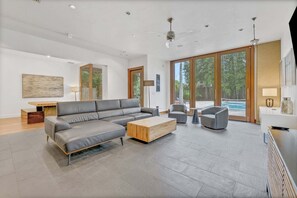 Ein modernes Wohnzimmer mit einem Ecksofa, einem Couchtisch und Blick auf einen Pool.