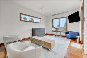 A modern living room with a flat-screen TV, a wooden coffee table, a white sofa, a blue armchair, and a dining area with a table and chairs. - Rooftop Oasis in Historic St. Augustine Panoramic Intracoastal Waterway Views (St. Augustine)