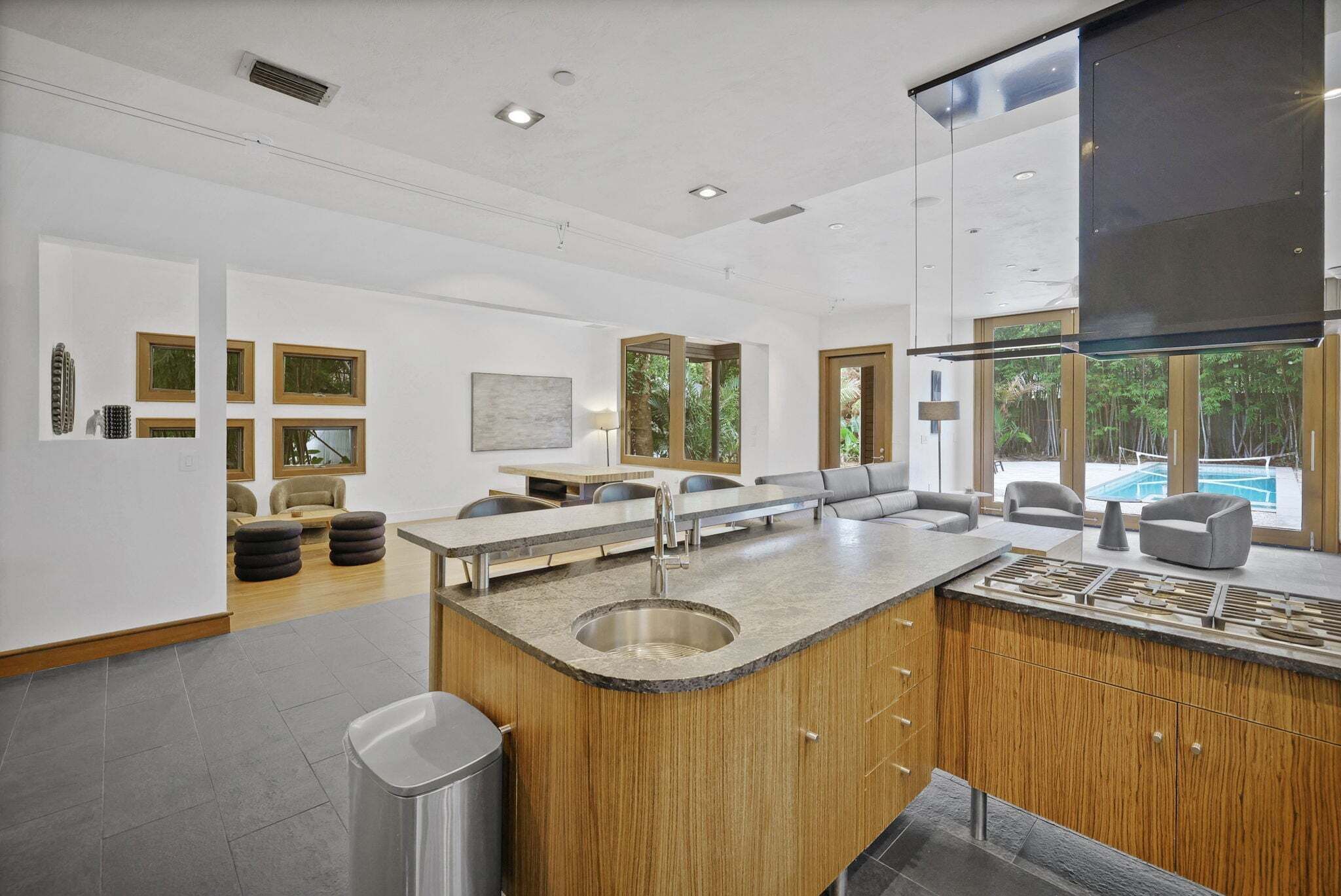 Une cuisine moderne dotée d’un îlot central, de meubles en bois et offrant une vue sur une piscine.