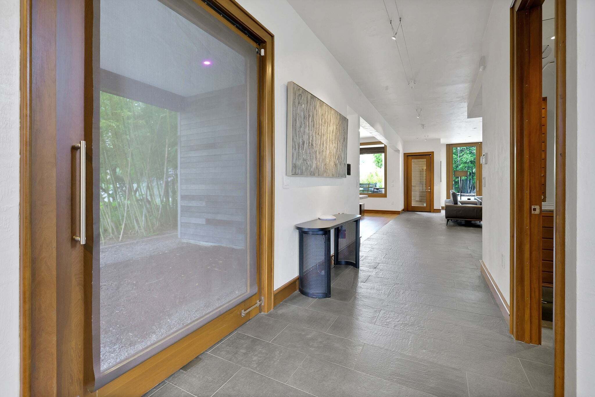 A hallway with a sliding glass door, a bench, and a painting on the wall.