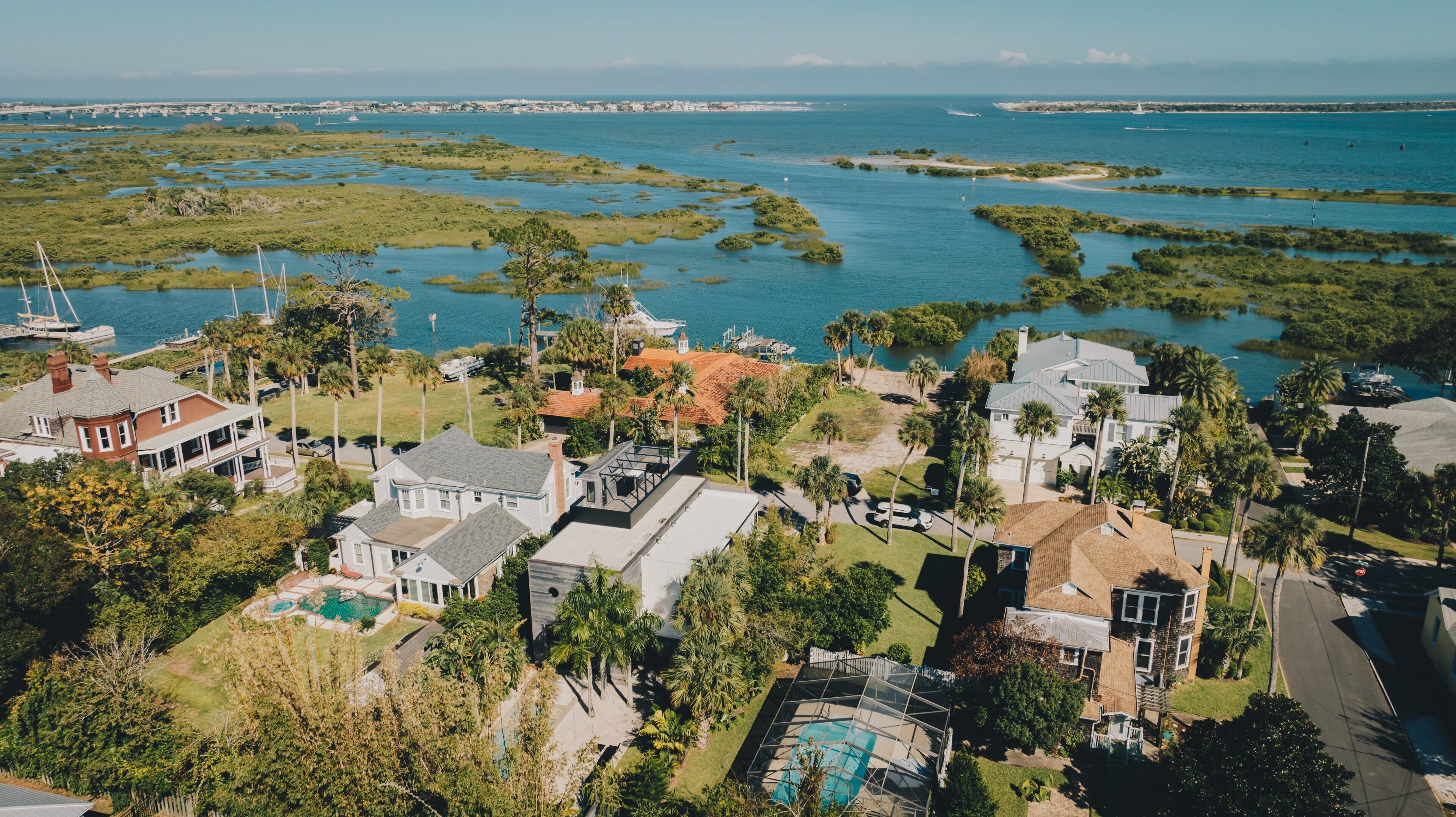 Vue aérienne d’un quartier résidentiel situé sur la côte, avec des maisons, une piscine et un port de plaisance.