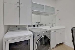 A laundry room with a front-loading washer and dryer, a sink, and cabinets. - Rooftop Oasis in Historic St. Augustine Panoramic Intracoastal Waterway Views (St. Augustine)
