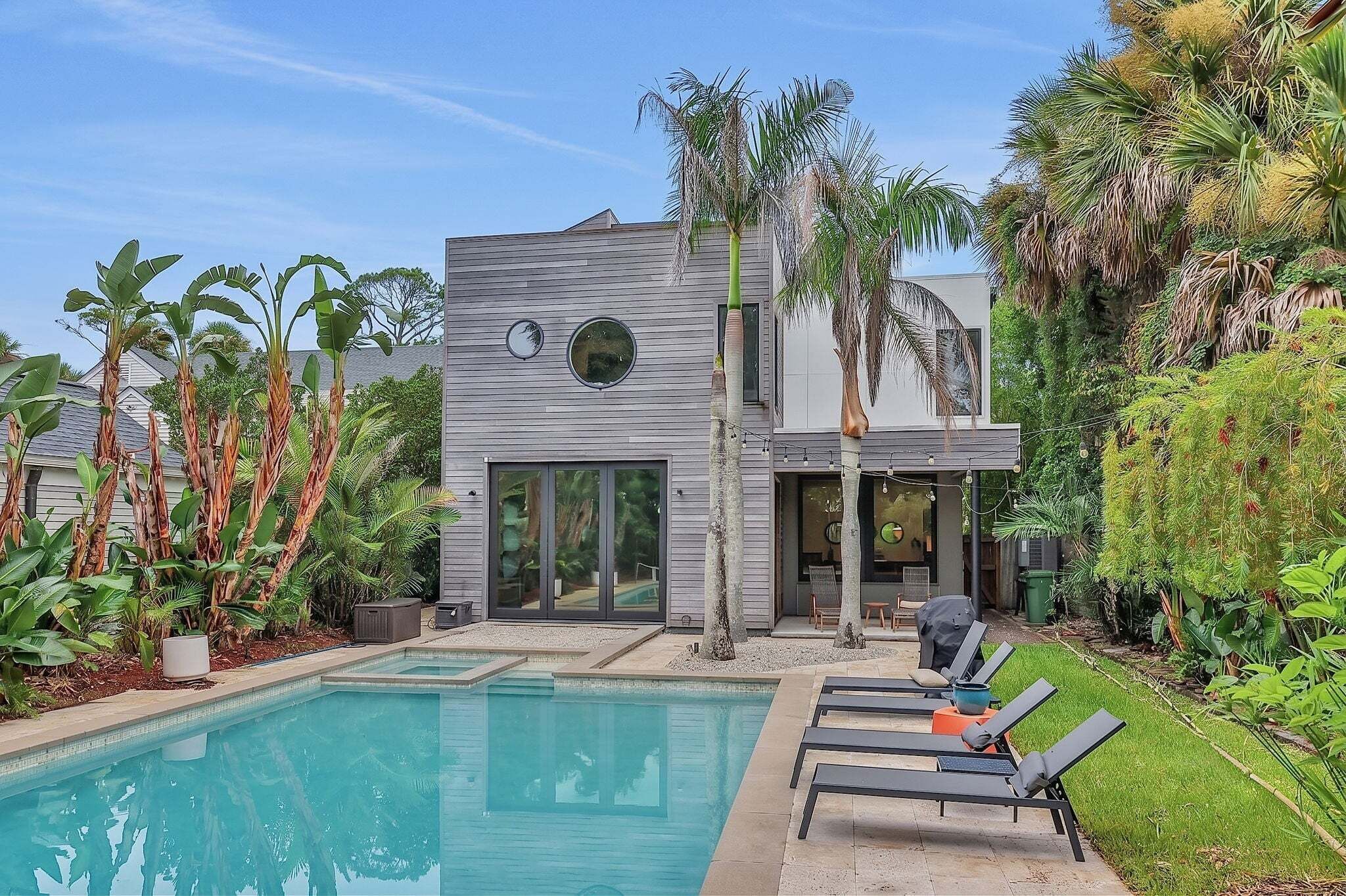 Una casa moderna con piscina, mobiliario exterior y exuberante vegetación tropical.