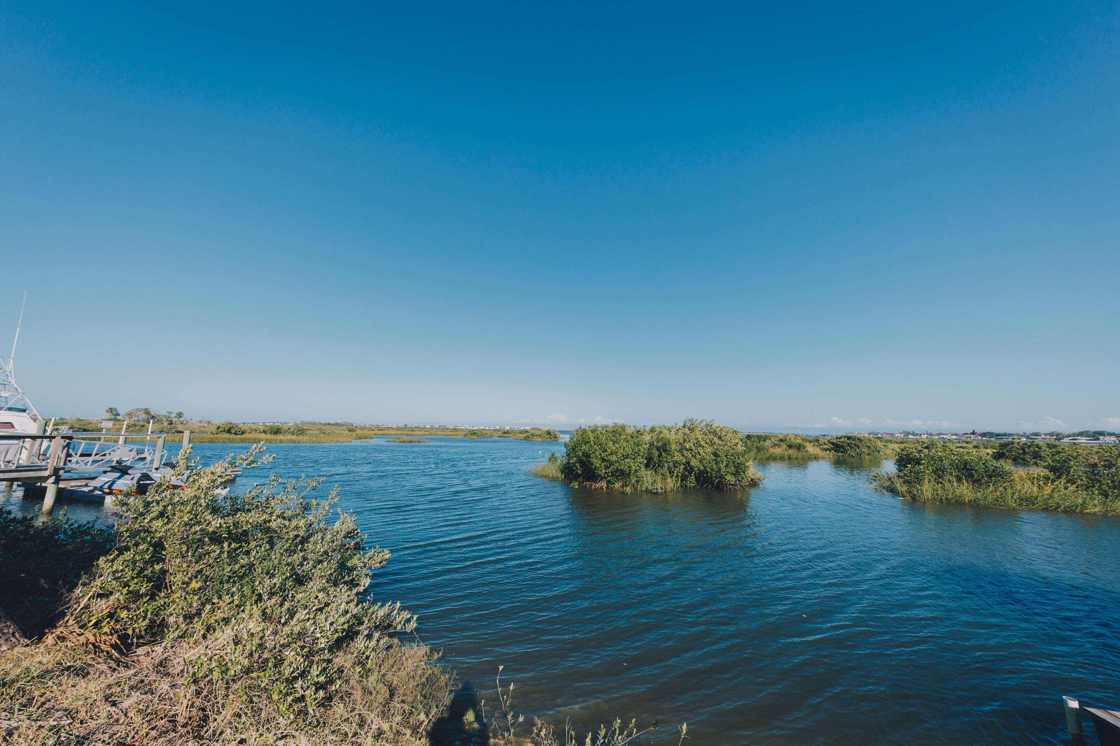 Un plan d’eau calme où sont amarrés des bateaux, le tout entouré de végétation.
