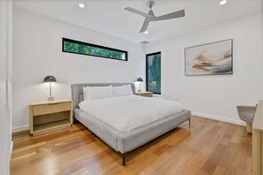 A modern bedroom with a bed, a nightstand, a desk, a chair, a ceiling fan, and artwork on the walls. - Rooftop Oasis in Historic St. Augustine Panoramic Intracoastal Waterway Views (St. Augustine)